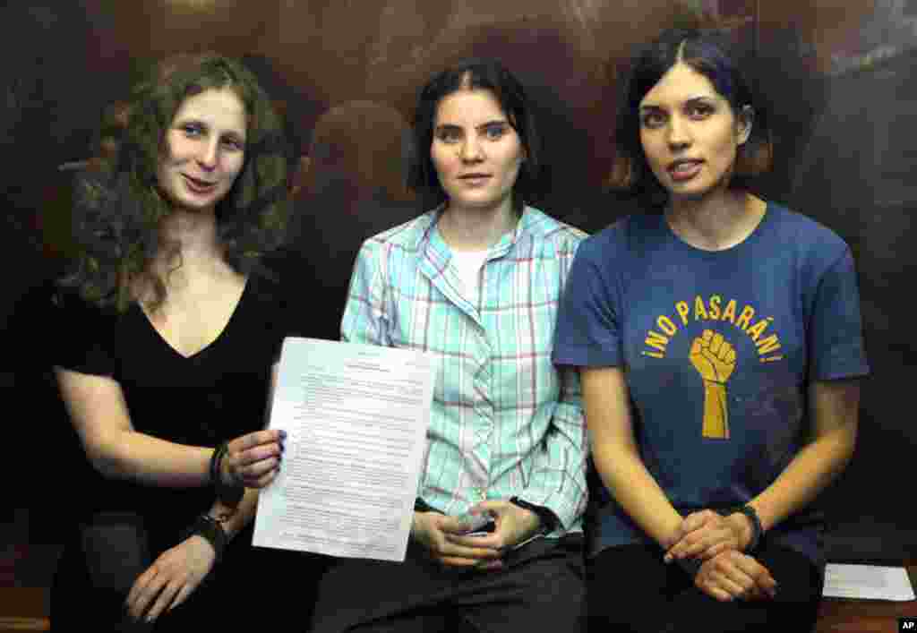 Thành viên của ban Pussy Riot. Từ trái: Maria Alekhina, Yekaterina Samutsevich, và Nadezhda Tolokonnikova cầm bản án trong khi ngồi bên trong một phòng kiếng trong một tòa án ở Moscow