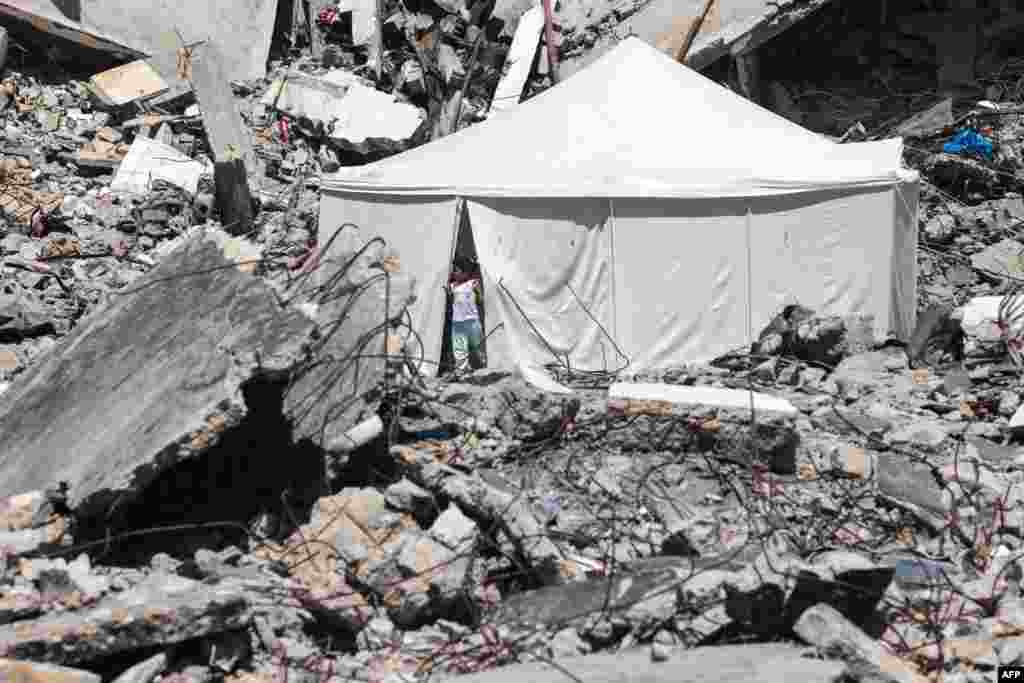 A displaced Palestinian stands at the entrance of a tent set up amid the rubble of a building damaged during Israeli bombardment in Rafah, on the southern Gaza Strip.