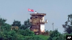 ແຟ້ມຮູບ-ທະຫານເກົາຫຼີເໜືອຄົນນຶ່ງ ຢືນຢູ່ປ້ອມຍາມກອງທັບ ຂອງເກົາຫຼີເໜືອ ໃນຂະນະທີ່ທຸງຂອງເກົາຫຼີເໜືອ ປິວໄປມາຕາມລົມ, ຮູບພາບທີ່ຖ່າຍຈາກເມືອງ ເປຈູ, ເກົາຫຼີໃຕ້, ວັນທີ 24 ກໍລະກົດ 2024.