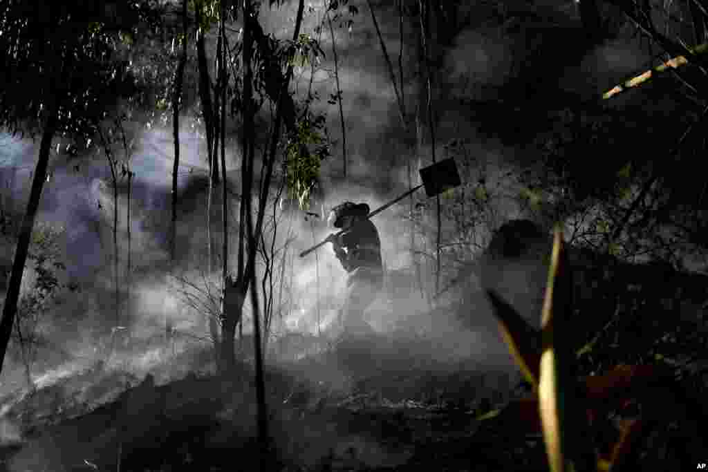 A firefighter walks through the smoke of a mountain fire in Soacha near Bogota, Colombia, Aug. 14, 2023.