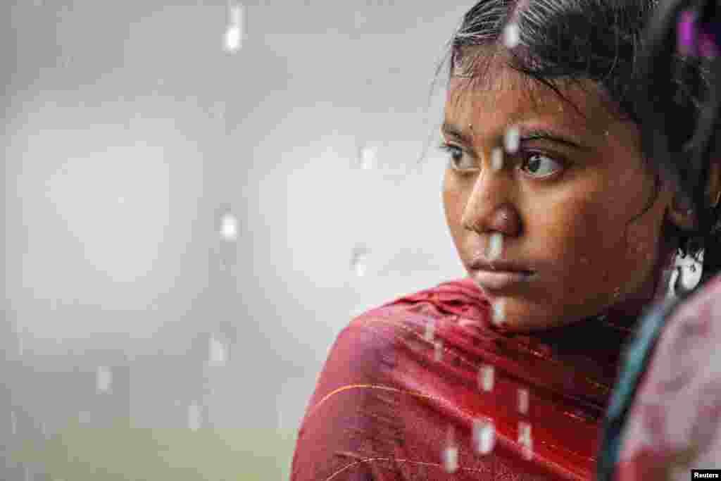 A girl looks on as she takes shelter under a shed during a downpour in Dhaka, Bangladesh, Aug. 29, 2023.