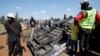 People stand next to a police vehicle that was burned during a demonstrations against the Kenya's proposed finance bill in Nairobi, Kenya, June 26, 2024. 
