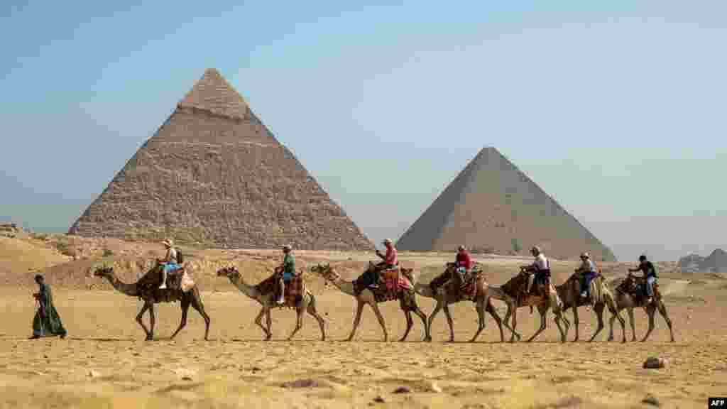 A guide pulls a lead camel as tourists ride in a row past the pyramids at the Giza Pyramids Necropolis on the outskirts of Giza, Egypt.