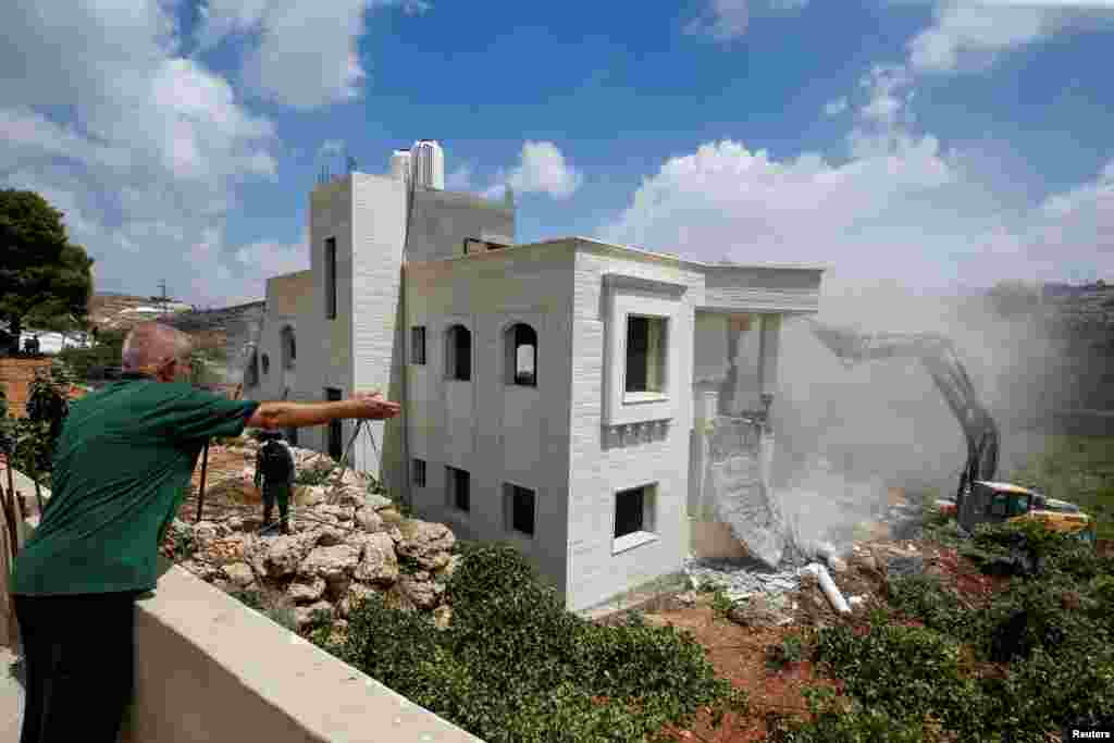 A Palestinian man gestures as an Israeli machinery operator guarded by Israeli forces demolishes a Palestinian house in Hebron in the Israeli-occupied West Bank.
