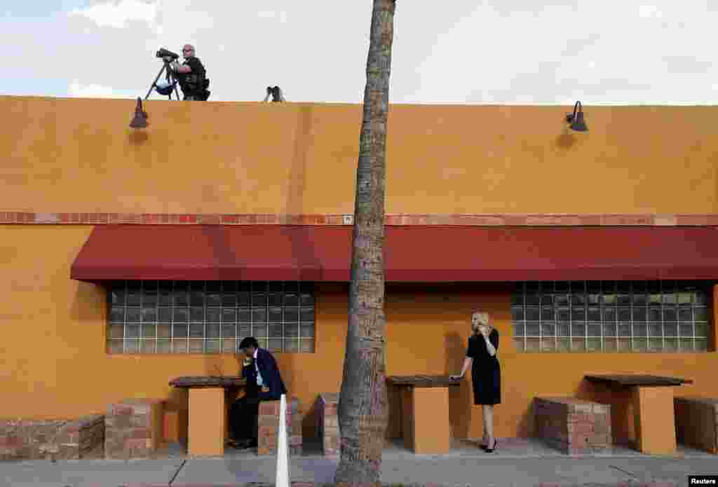 U.S. President Joe Biden’s director of speech writing Vinay Reddy works at his laptop and White House economic advisor Lael Brainard talks on her phone as members of the Secret Service keep watch atop a Mexican restaurant where Biden was holding a campaign event in Phoenix, Arizona, March 19, 2024.