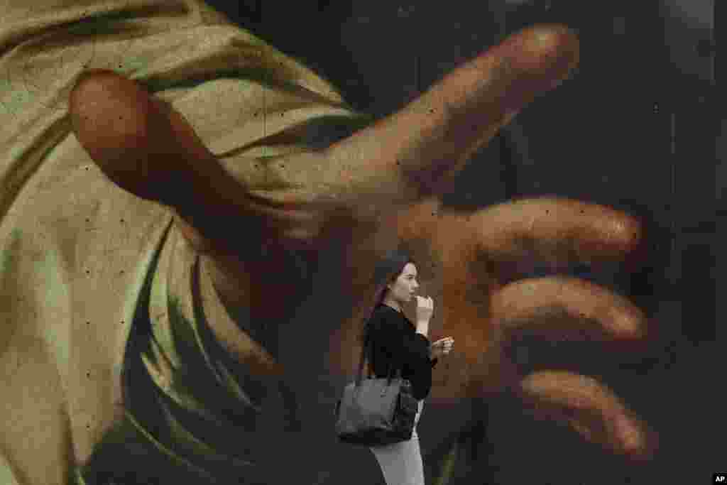 A woman walks past a poster featuring the painting of Caravaggio's "The Supper at Emmaus" outside the National Gallery, in London.
