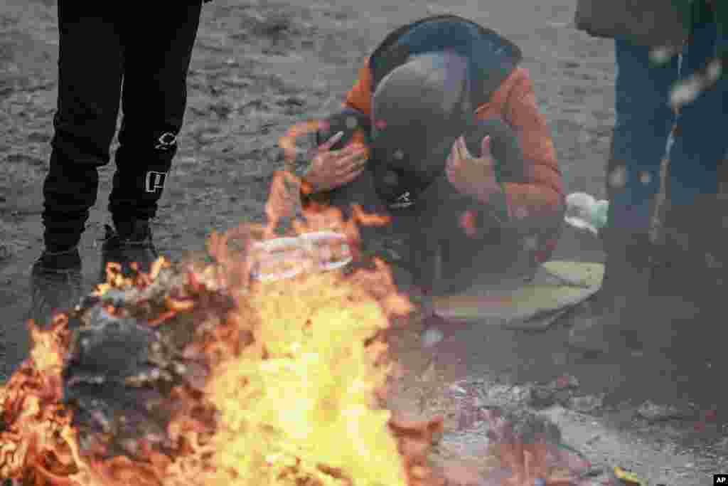 Refugees fleeing conflict in Ukraine warm up near a fire after arriving at the Medyka border crossing in Poland, Feb. 28, 2022.