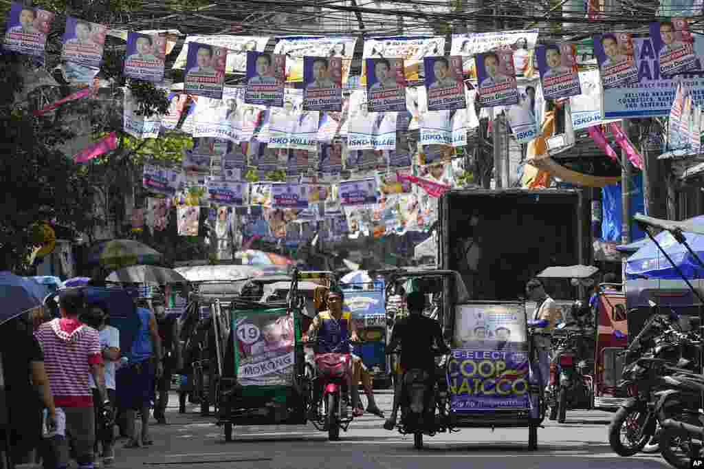 Residents pass by election campaign posters near a polling center in Manila, Philippines. The country prepares to vote for its new leader next week.