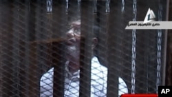 FILE - In this image taken from Egypt State TV, Mohammed Morsi stands inside a glass-encased metal cage in a courtroom in Cairo, Jan. 28. 2014. 