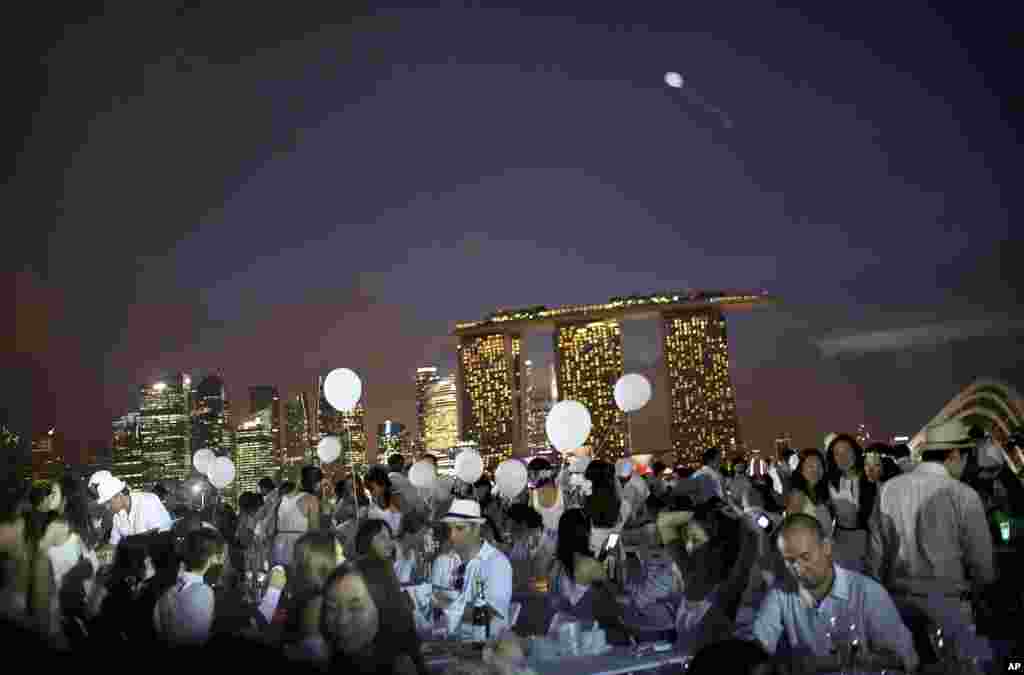 Para tamu duduk menikmati hidangan malam berlatar belakang Pantai Marina dan gedung-gedung pencakar langit pusat keuangan Singapura di Marina Barrage, Singapura. Diner en Blanc atau Makan Malam Putih yang dimulai di Paris 25 tahun yang lalu, kini memasuki tahun kedua di Singapura. Para tamu diharapkan untuk berpakaian warna putih dan membawa makanan sendiri, meja dan kursi untuk menikmati santap malam bersama secara "flash mob" di lokasi rahasia yang informasinya hanya disebarkan beberapa menit sebelum acara dimulai.