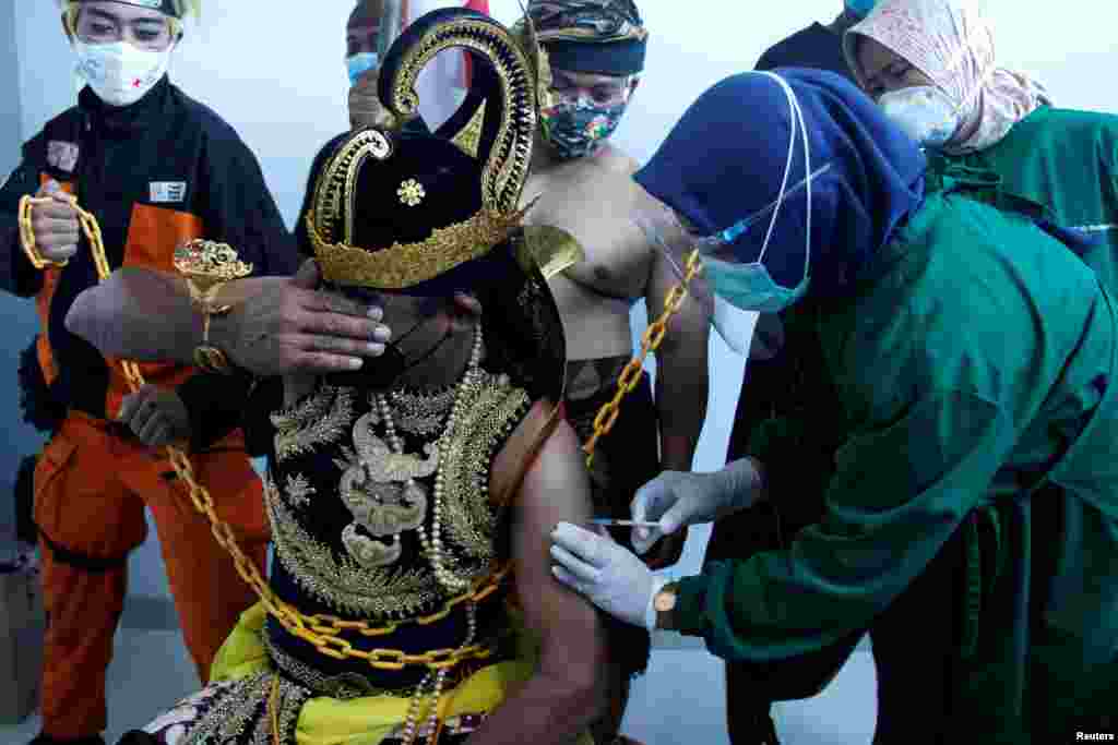 Seorang petugas medis menyuntikkan vaksin Sinovac kepada seorang pria yang mengenakan kostum 'Wayang', saat Indonesia melakukan vaksinasi massal Covid-19 di sebuah rumah sakit di Solo, Jawa Tengah, 22 Januari 2021. (Foto: Maulana Surya / Antara via Reuters)