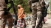 FILE - A woman walks past Nigerian soldiers at a checkpoint in Gwoza, Nigeria, a town newly liberated from Boko Haram, April 8, 2015. 