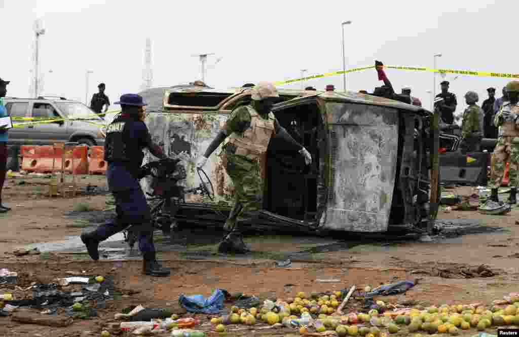 Seorang tentara dan seorang perwira paramiliter membantu memindahkan bagian dari sebuah mobil rusak di lokasi serangan bom mobil di Nyanya, Abuja, Nigeria. 