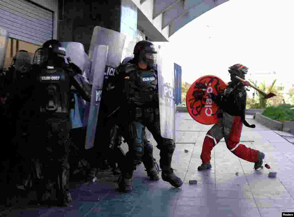 A demonstrator raises an axe towards riot police during anti-government protests, as Colombia commemorates Independence Day in Bogota, July 20, 2021.