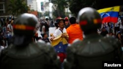 An opposition supporter holds a national flag as she shouts at the riot police during a protest against President Nicolas Maduro's government in Caracas, Feb. 17, 2014.