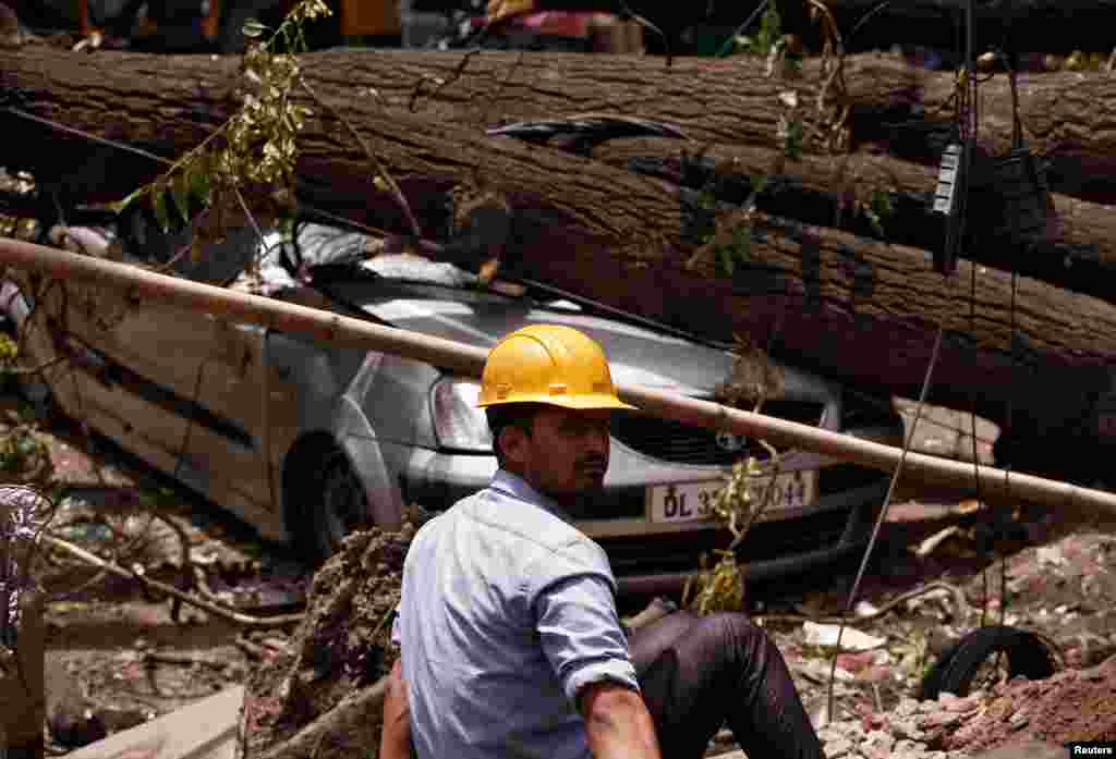 An electric utility worker rests next to uprooted trees after dust storms tore through the city Tuesday night, in New Delhi, India.