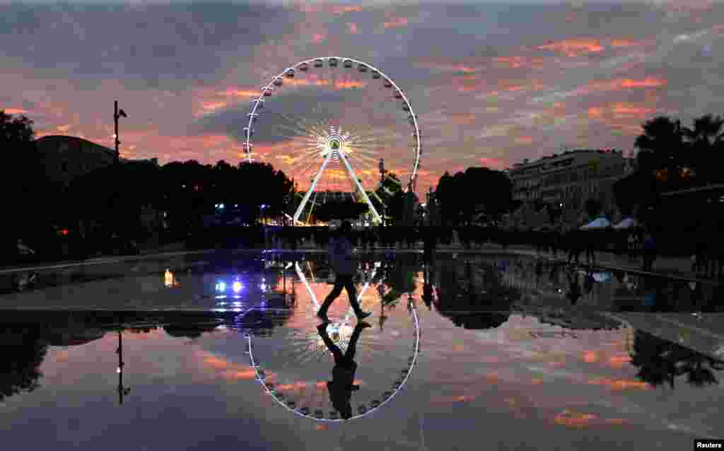 A man is reflected in the water of a fountain as he walks past a Ferris wheel during Christmas holiday season illuminations in Nice, France.