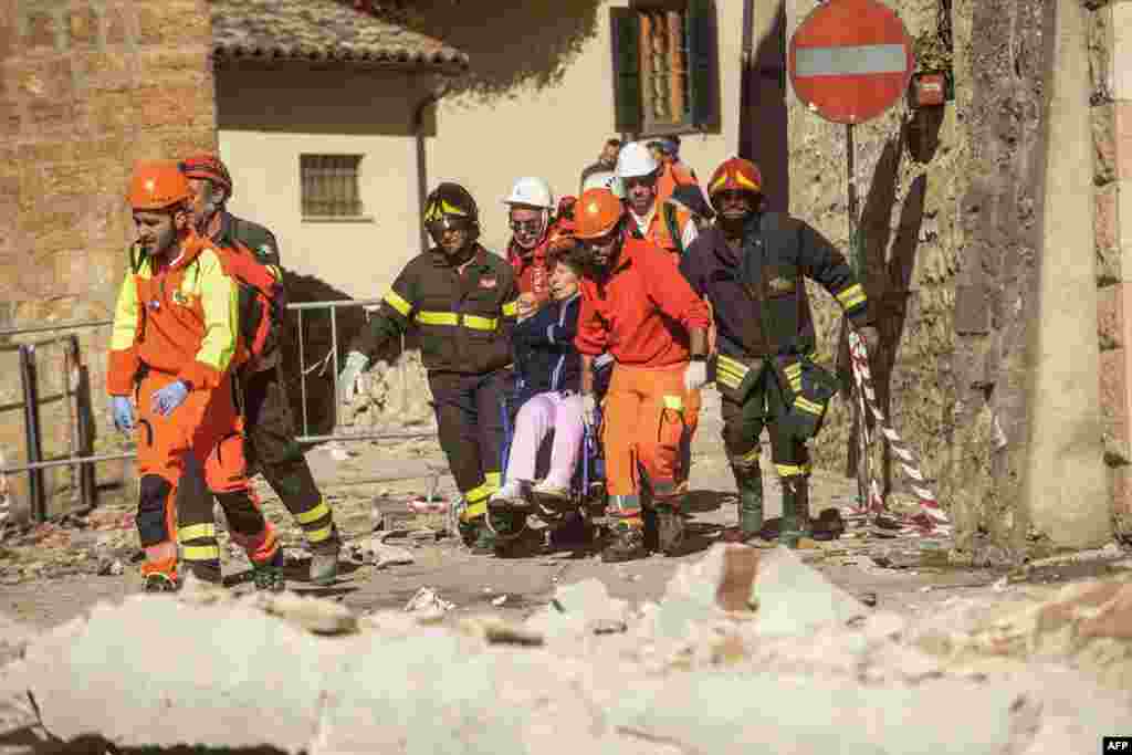 Para petugas pemadam kebakaran dan penyelamat menggotong perempuan berkursi roda menyusul gempa di Norcia, Italia (30/10). (AFP/Fabrizio Troccoli)
