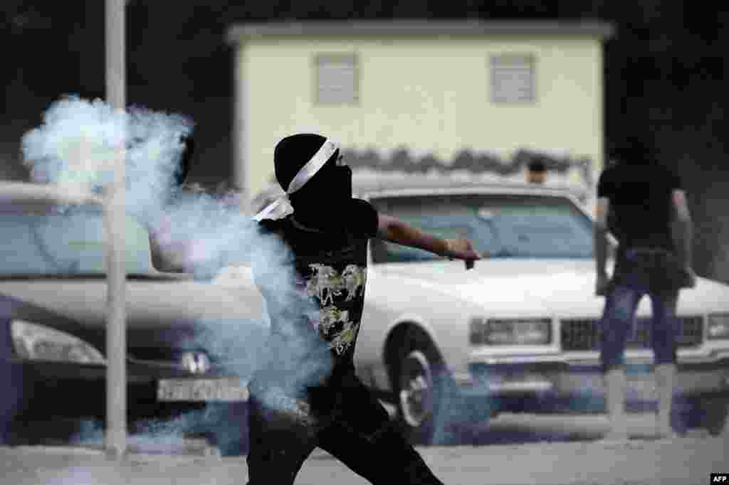 A Bahraini protester throws back a tear gas canister during clashes with riot police following an anti-regime demo heading to 'Pearl Square' after a religious procession marking Ashura in the village of Daih, Bahrain.