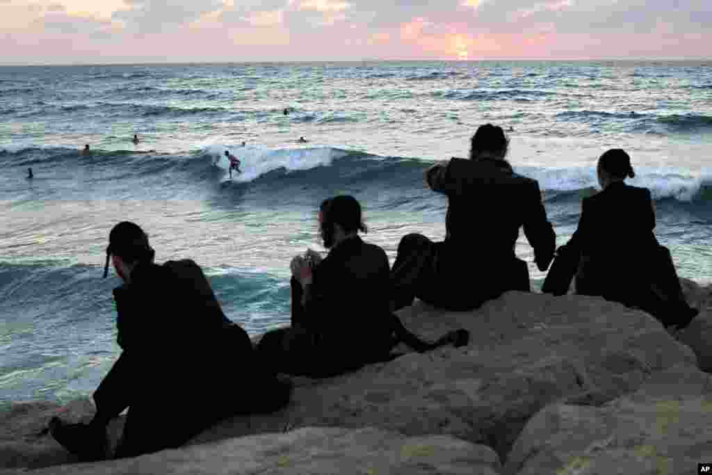 Para pria Ultra-Ortodoks Yahudi menonton para peselancar selama hari libur di kota pelabuhan Ashdod, Israel selatan.