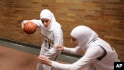 FILE - Fordson High School basketball player Fatima Kobeissi, (11) warms up in the hallway with teammate Hyatt Bakri before the basketball game against Willow Run in Dearborn, Mich., in 2007. FIBA announced hijabs will be allowed in international competition.