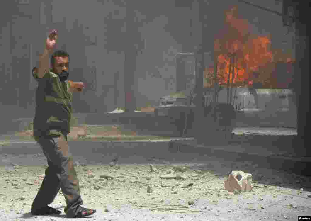 A man points towards a burning car, caused by what activists said was shelling by forces loyal to Syria's President Bashar al-Assad, Damascus, July 23, 2013.