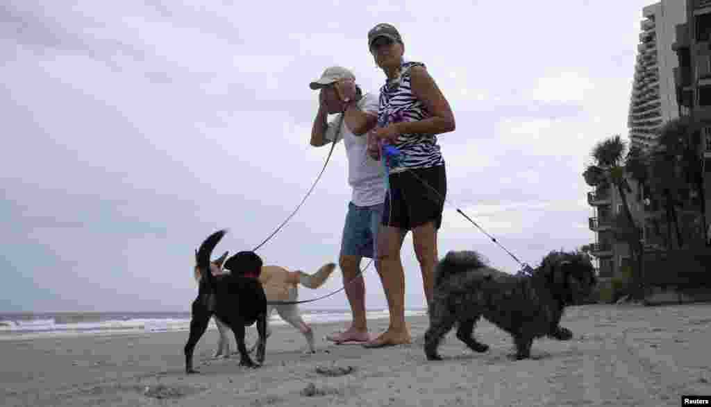 Bob Jenkins memegang topinya saat bersama kawannya Darlene Pittman membawa anjing mereka berjalan-jalan di tengah angin dari Badai Arthur yang semakin kencang di Pantai Surfside, South Carolina (3/7). (Reuters/Randall Hill)