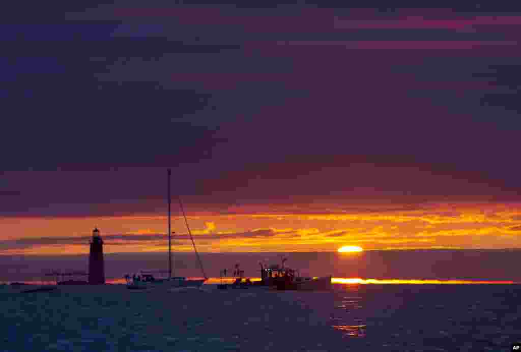 Sebuah perahu pencari lobster dan sebuah perahu layar tampak melalui Ram Island Ledge Light, mercusuar di Pelabuhan Portland, Cape Elizabeth, Maine, Amerika.