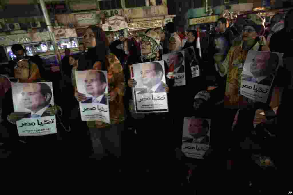 Para pendukung mantan komandan angkatan darat Abdel-Fattah el-Sissi memegang poster dirinya yang bertuliskan dalam huruf Arab "Hidup Mesir" saat menonton siaran wawancaranya dari layar besar di Kairo (5/5). (AP/Khalil Hamra)