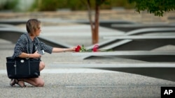 A woman reaches out to touch flowers placed on one of the benches of the Pentagon Memorial at the Pentagon, outside Washington, Sept. 11, 2014.