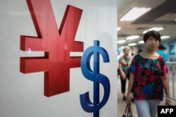 FILE - A woman walks past a yuan (L) and a US dollar (R) currency sign in Hong Kong on August 13, 2015.