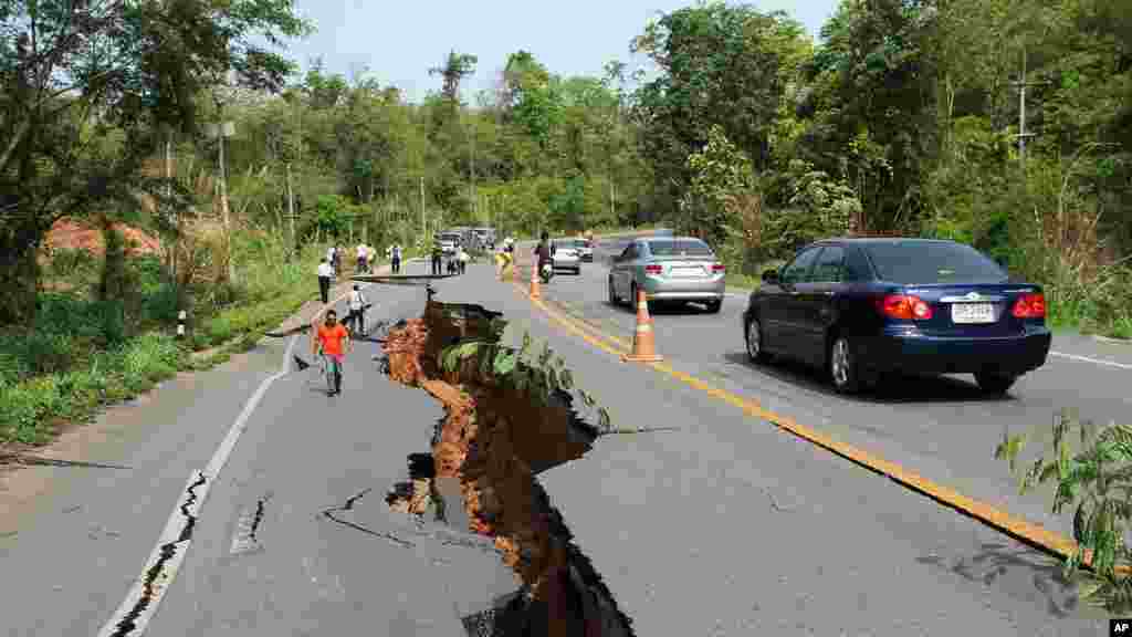 Pengendara motor melalui jalan raya yang retak selagi orang-orang mengamati kerusakan yang ditimbulkan oleh gempa bumi, Chiang Rai, Thailand utara, 6 Mei 2014.
