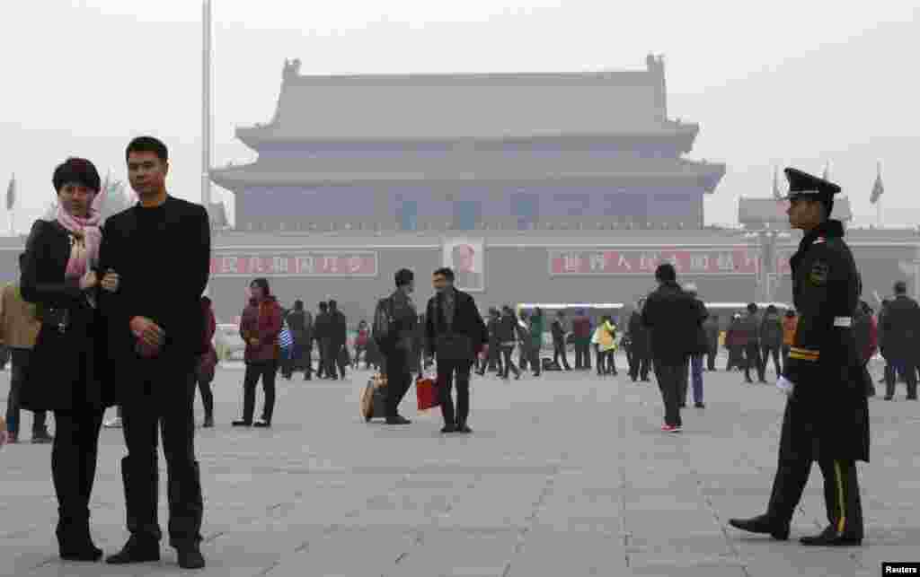 A paramilitary soldier patrols near visitors posing for souvenir pictures at Tiananmen Square, Beijing, China, Nov. 1, 2013.