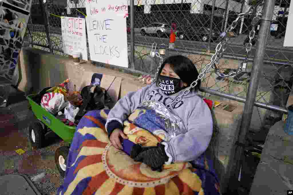 Kia Hirt sits with a chain attached to a fence while protesting outside the Hennepin County Government Center in Minneapolis, Minnesota, where the trial for former police officer Derek Chauvin continues. Chauvin is charged with murder in the death of George Floyd during an arrest last May in Minneapolis. 