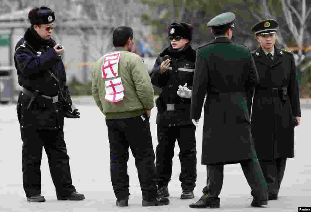 Seorang laki-laki dengan kertas bertuliskan 'demokrasi' di punggungnya ditanyai oleh polisi dekat Balai Sidang Rakyat di Alun-alun Tiananmen, Beijing tengah, Tiongkok.