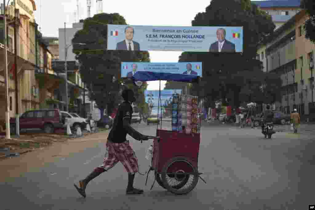 A Guinean street vendor pushes his cart under banners featuring French President Francois Hollande and his Guinean counterpart Alpha Conde in Conakry, Guinea, Wednesday, Nov. 26, 2014.