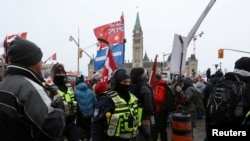 FILE - Maafisa wa polisi wakiwa na waandamanaji mbele ya jengo la Bunge wakati wenye magari na wafuasi wao wanaopinga masharti ya COVID-19 na kuchanja, Ottawa, Canada, Feb. 6, 2022.