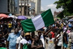 People hold banners as they demonstrate on the street to protest against police brutality, in Lagos, Nigeria, Tuesday Oct. 20, 2020. After 13 days of protests against police brutality, authorities have imposed a 24-hour curfew in Lagos Nigeria's…