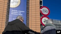 Two people are seen underneath a giant banner for the euro currency outside an EU summit in Brussels, Nov. 22, 2012. 
