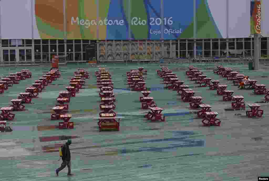 Seorang pria berjalan melewati Taman Olimpiade pada saat hari hujan di Rio de Janeiro, Brazil.