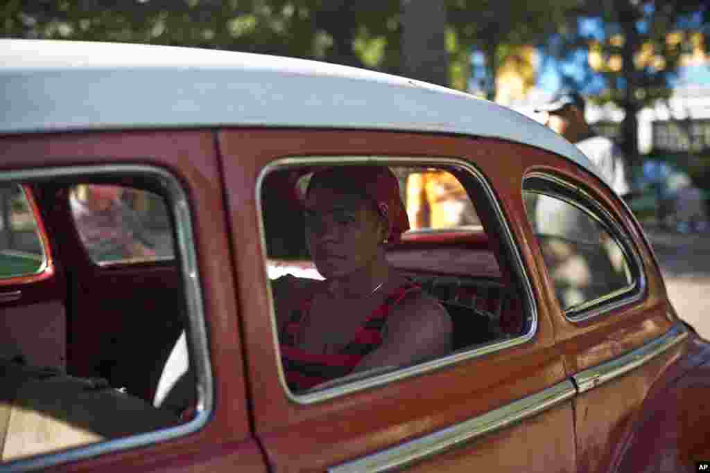 Seorang perempuan menunggu di dalam mobil klasik Amerika yang dulu digunakan sebagai angkutan umum di Havana, Kuba (18/12). (AP/Ramon Espinosa)