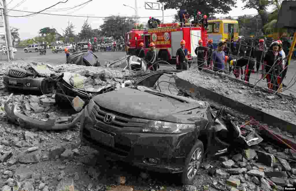 Petugas pemadam kebakaran berdiri dekat mobil-mobil yang hancur akibat gempa di kota Cebu, Filipina tengah (15/10).