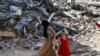 Seorang perempuan dan anak-anak berjalan di antara reruntuhan bangunan di kamp pengungsi Nuseirat di Gaza tengah, pada 9 Juni 2024. Bangunan kamp hancur akibat serangan Israel ke area tersebut. (Foto: Reuters/Abed Khaled)