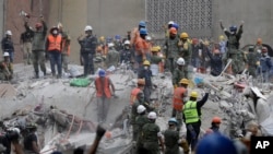 FILE - Rescue workers, some holding their arms up as a sign to maintain silence, search for survivors at a building that collapsed during an earthquake in Mexico City, Mexico, Sept. 21, 2017.