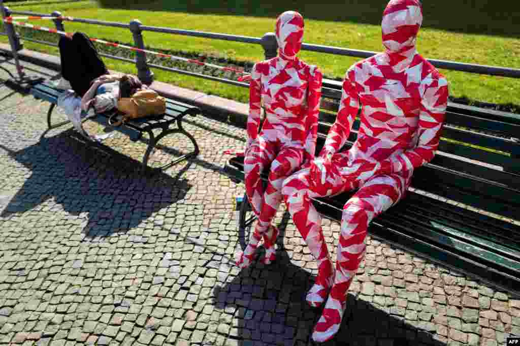 A woman takes a nap on a bench next to mannequins wrapped in barrier tape near Berlin's landmark Brandenburg Gate as part of German artist Dennis Josef Meseg's Corona Memorial called "It is Like it is."