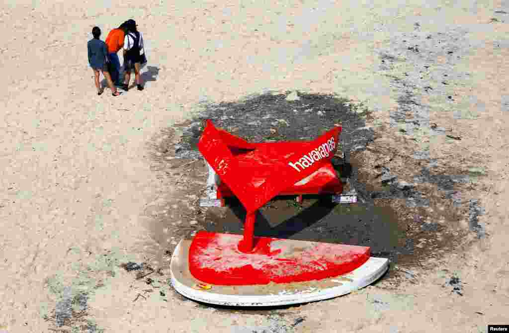 Tiga orang berdiri di dekat patung yang rusak akibat diterjang ombak besar di pantai Tamarama, Sydney, Australia.