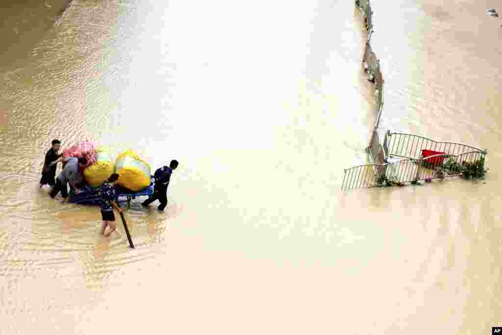 Residents move their belongings across a flooded street in Zhengzhou in central China's Henan province. (Credit: Xinhua News Agency)