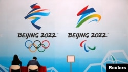 Staff members sit near a board with signs of the 2022 Olympic Winter Games, at the National Aquatics Center, known colloquially as the "Ice Cube", in Beijing, China, April 1, 2021.