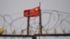 FILE - The Chinese flag flutters behind razor wire at a housing compound in Yangisar, south of Kashgar, in China's western Xinjiang region, June 4, 2019.
